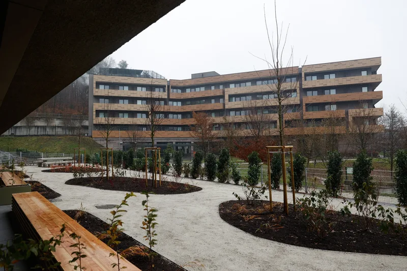Poti, klop in zasaditve pred oskrbovanimi stanovanji; v ozadju je DEOS Center starejših Črnuče.