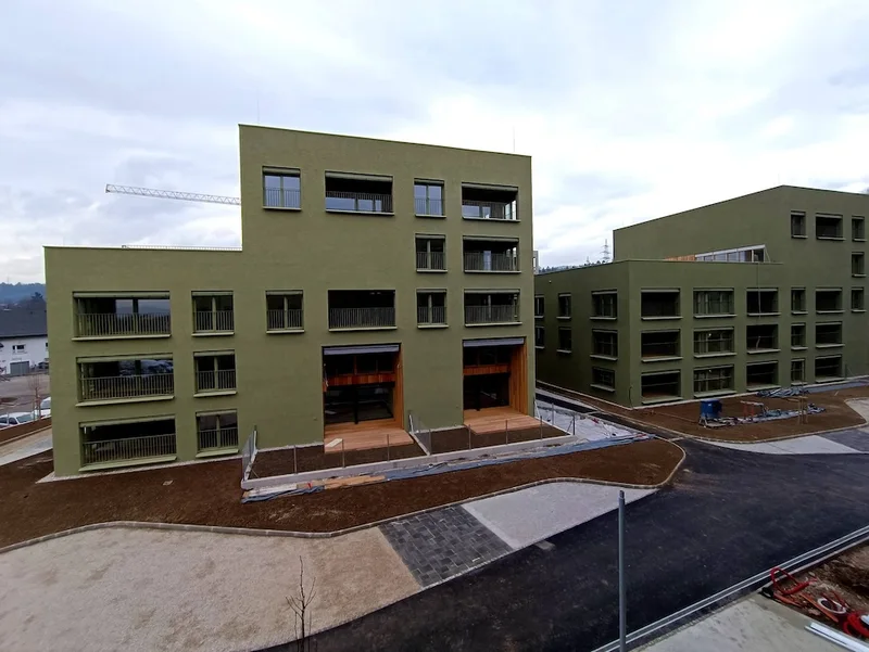 Dve zeleni stavbi ob zavitih poteh; v ospredju sta leseni terasi in še nezatravljene površine.