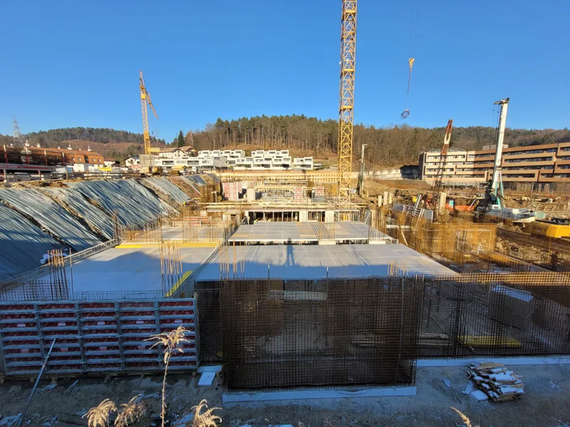 Pogled na gradbišče Lagom z betonskimi stenami, opaži in stolpnimi žerjavi.