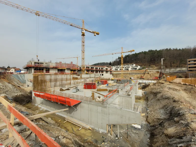 Pogled čez gradbišče z nastajajočimi stenami, opaži in delovnimi ploščadmi.